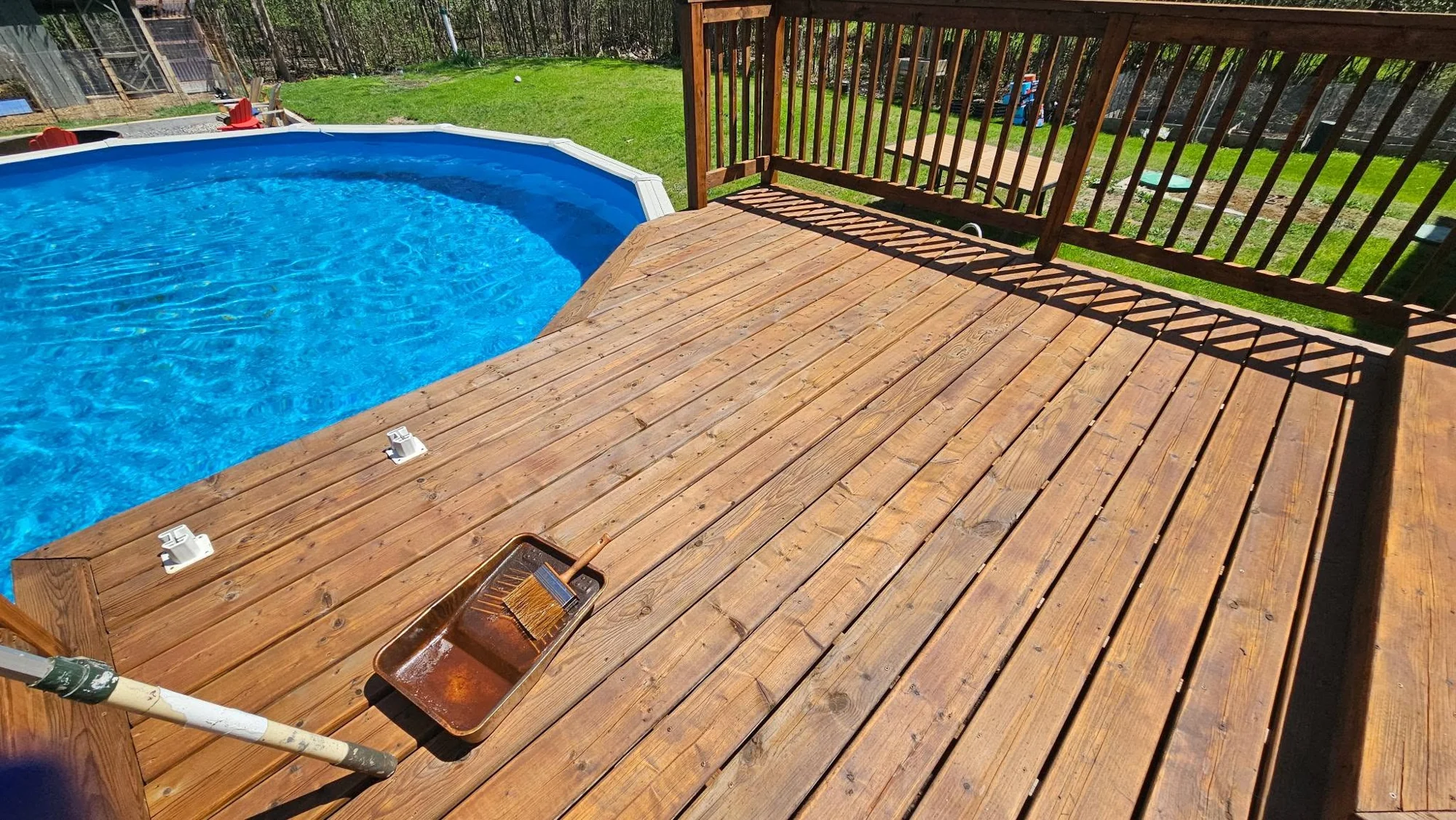 Application manuelle de teinture sur une terrasse en bois près d’une piscine.