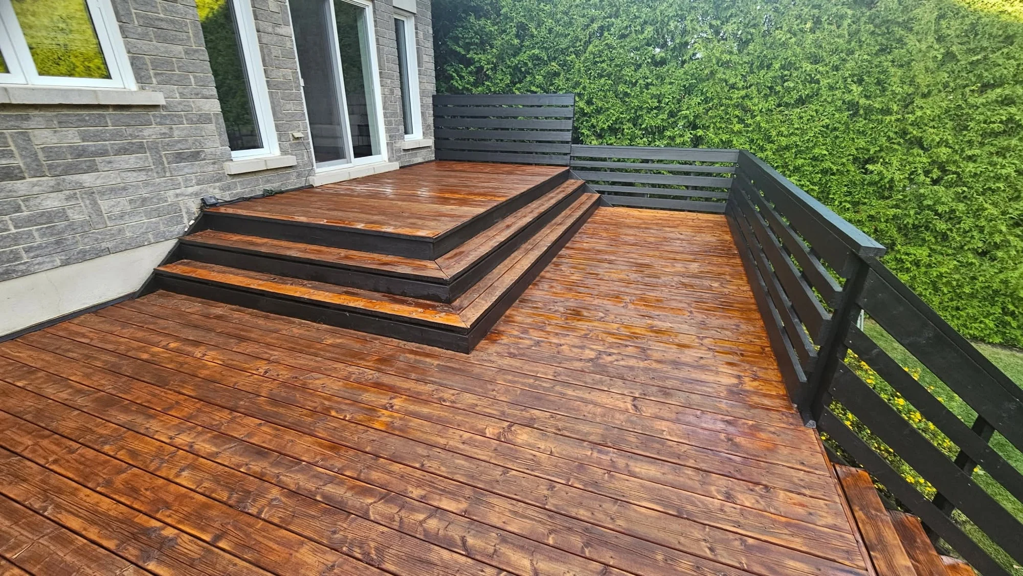 Terrasse restaurée au fini brun ambré, avec marches et rampe noire.